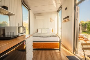 A bedroom with a bed, a desk with a microwave, and a view of the outdoors.