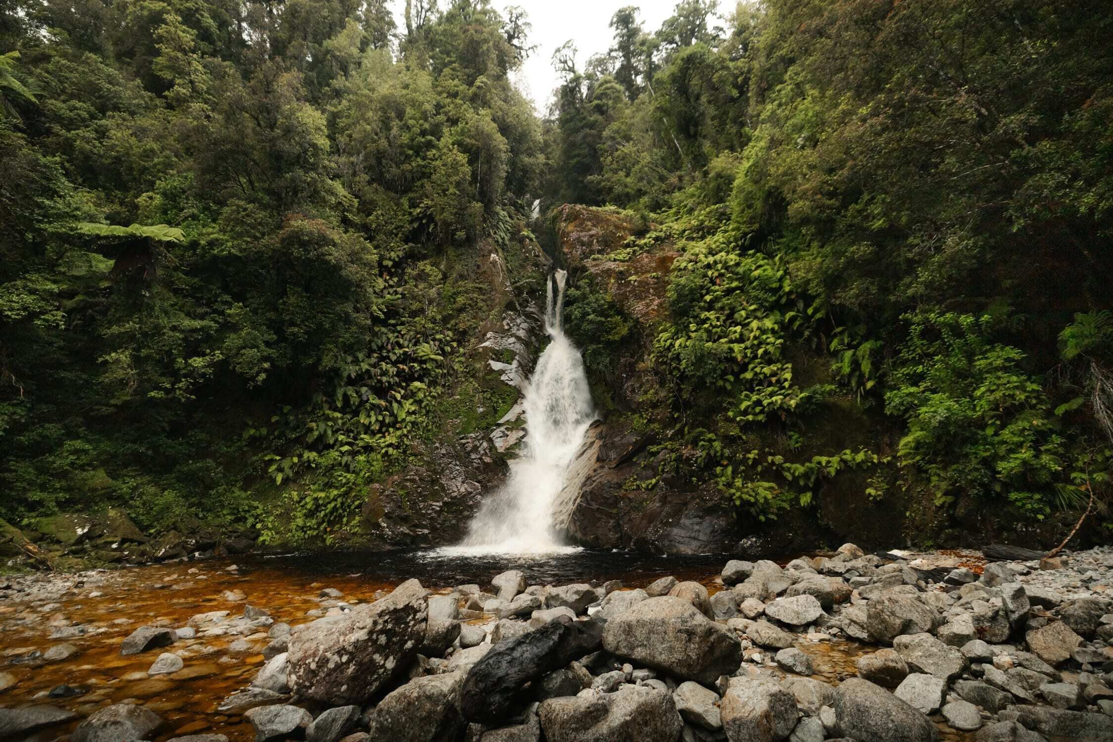 Een waterval in een bebost gebied met een rotsachtige voorgrond.