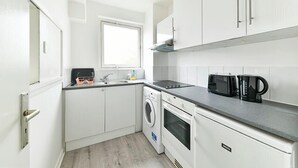 A compact kitchen with white cabinetry, a built-in oven, a microwave, and a washing machine. - The Elden - No.16 - Fairway Hosting (Greater London)
