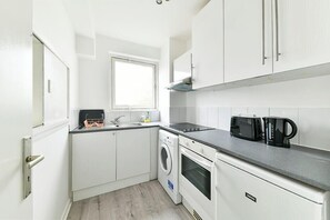 A compact kitchen with white cabinetry, a built-in oven, a microwave, and a washing machine. - The Elden - No.16 - Fairway Hosting (Greater London)