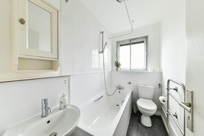 A modern bathroom with a bathtub, sink, toilet, and a window providing natural light. - The Elden - No.16 - Fairway Hosting (Greater London)