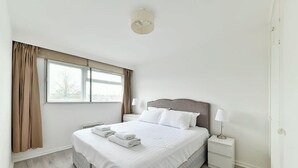 A hotel room with a large bed, a nightstand, a lamp, and a window with curtains. - The Elden - No.16 - Fairway Hosting (Greater London)