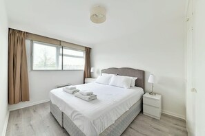 A hotel room with a large bed, a nightstand, a lamp, and a window with curtains. - The Elden - No.16 - Fairway Hosting (Greater London)