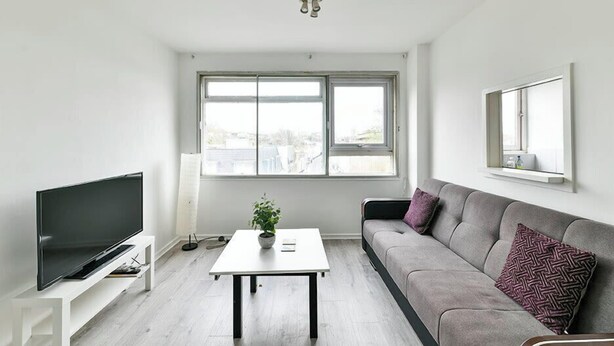 A modern living room with a flat-screen TV, a white coffee table, a grey sofa, and a large window providing a view of the outside. - The Elden - No.16 - Fairway Hosting (Greater London)