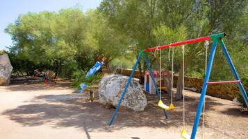 Ein Spielplatz mit Schaukeln, einer Rutsche und einem Felsen.
