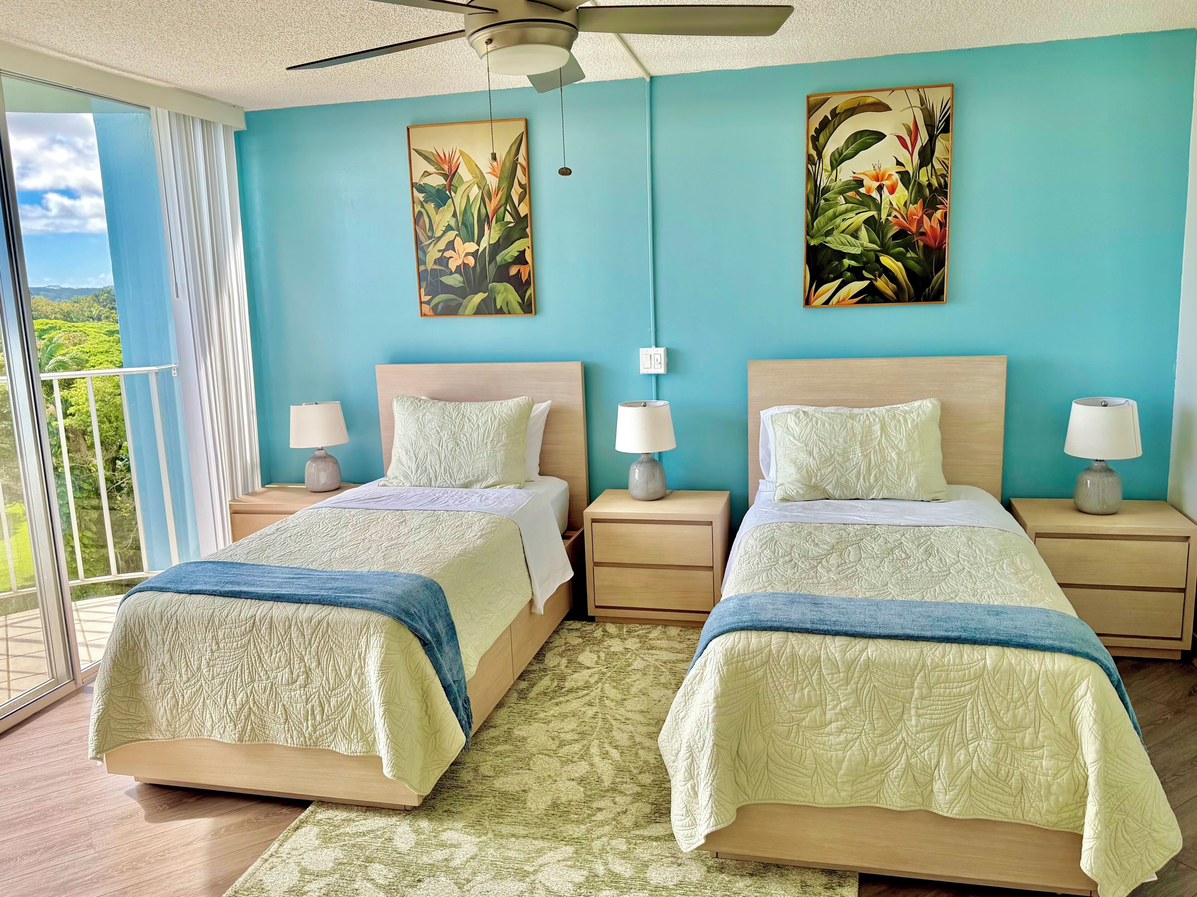 A bedroom with two beds, a ceiling fan, and a view of greenery through the window.
