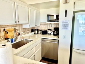 A kitchen with white cabinets, a stainless steel dishwasher, a microwave, and a coffee maker. - Ocean & Wailoa River Views - AC + Pool - 2BD/2BTH (Hilo)