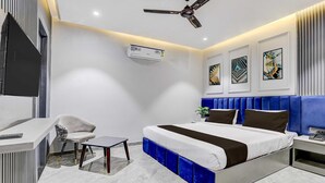 A modern hotel room with a bed, a desk, a chair, a ceiling fan, and artwork on the walls. - Suite Room Clubhouse Vytilla Kochi (Kanayannur)