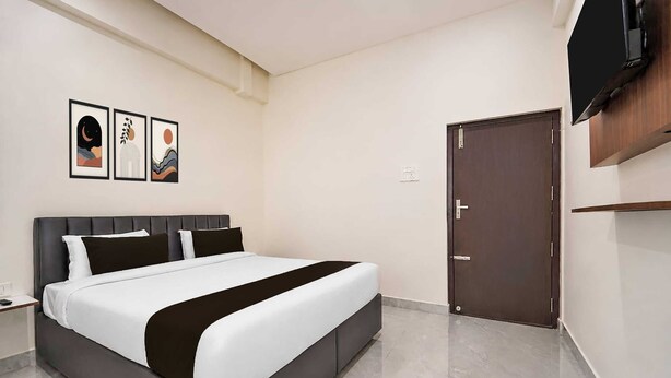 A modern hotel room with a large bed, a flat-screen TV mounted on the wall, and a door with a handle. - Suite Room Clubhouse Vytilla Kochi (Kanayannur)