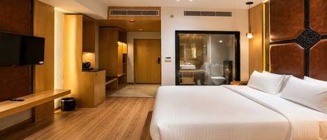 A modern hotel room with a large bed, a TV, a desk, and a bathroom.