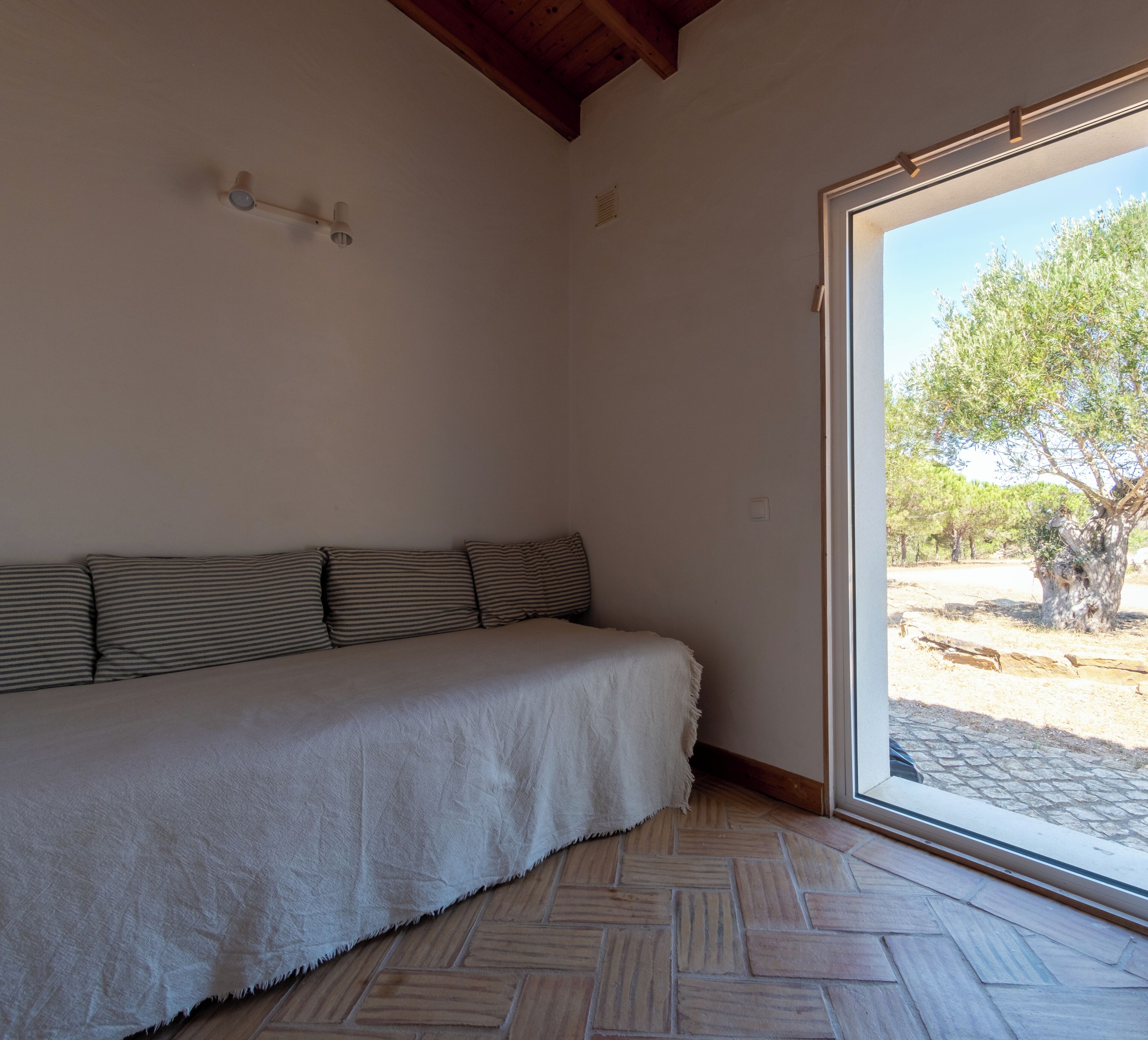 A room with a bed, a ceiling fan, a window, and a view of trees.