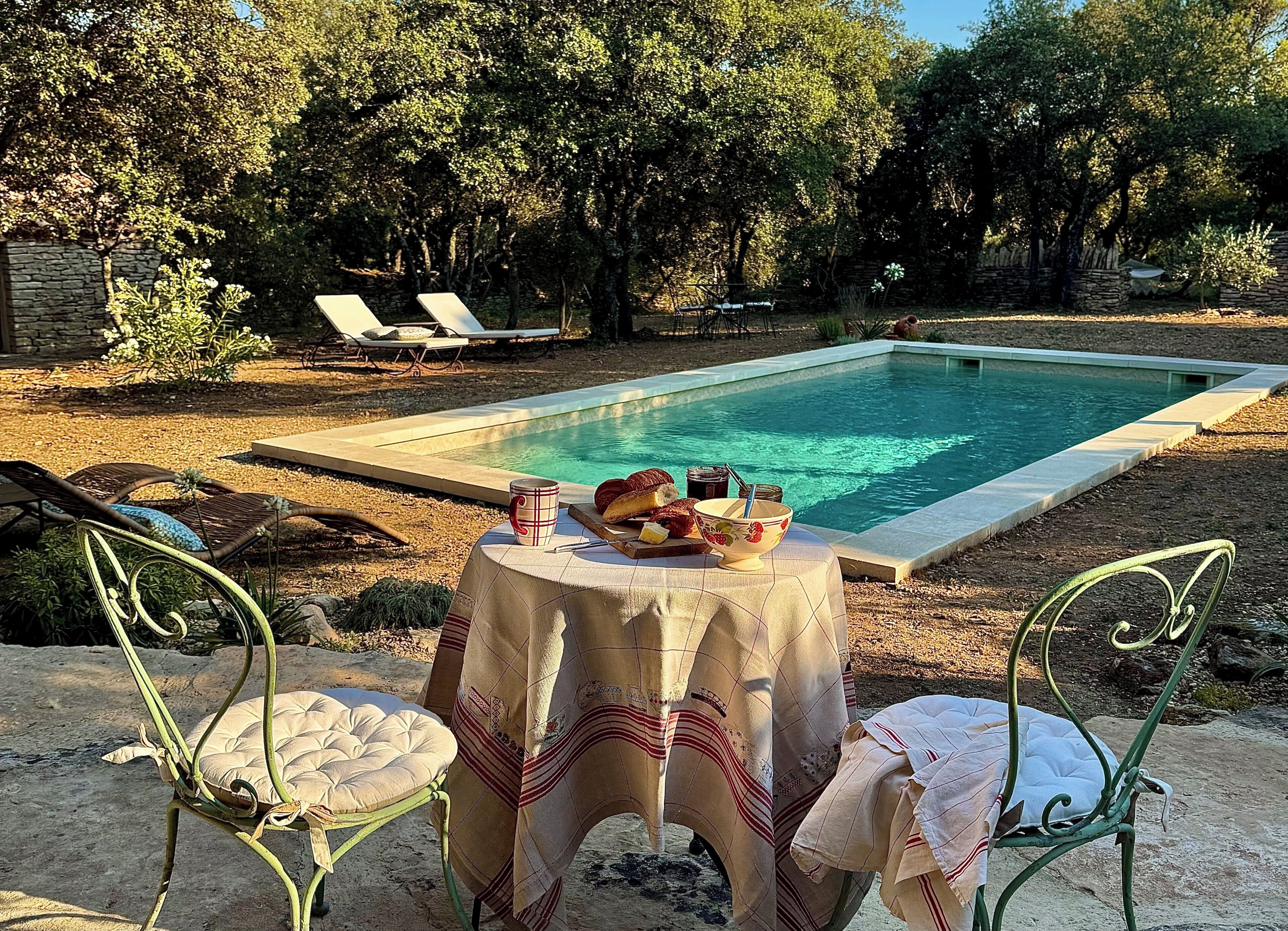 A poolside setting with a table set for a meal, surrounded by lounge chairs and a stone wall.
