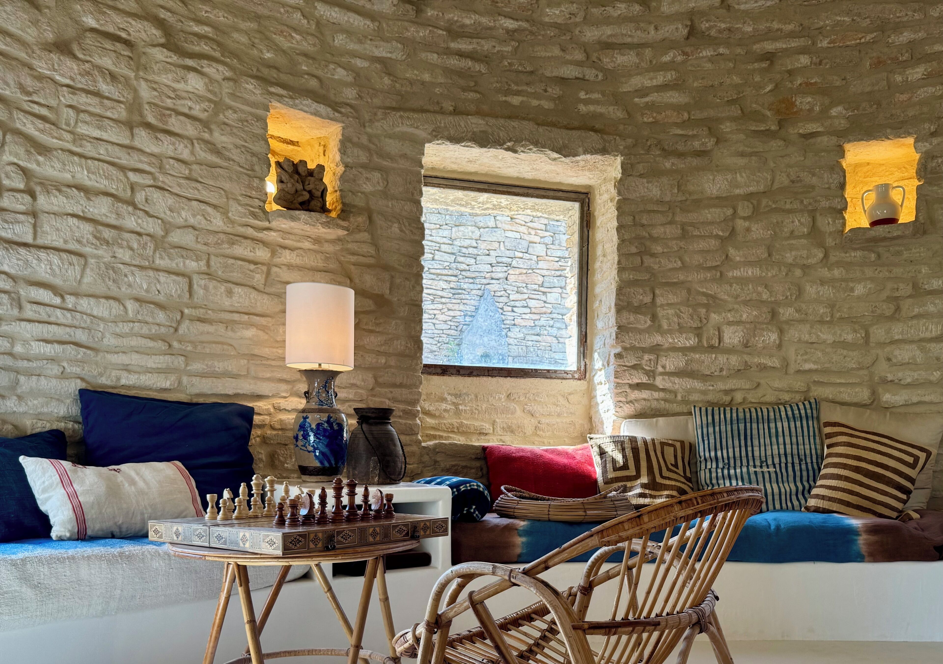 Una habitación de paredes de piedra con un tablero de ajedrez, una lámpara y una ventana.