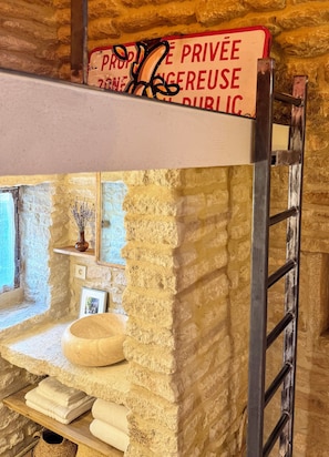 A rustic interior with a stone wall, a wooden shelf with towels, a small vase, and a ladder. - Les Cinq Bories - An Exceptional Estate Just a 10-Minute Walk from the Village of Gordes (Gordes)