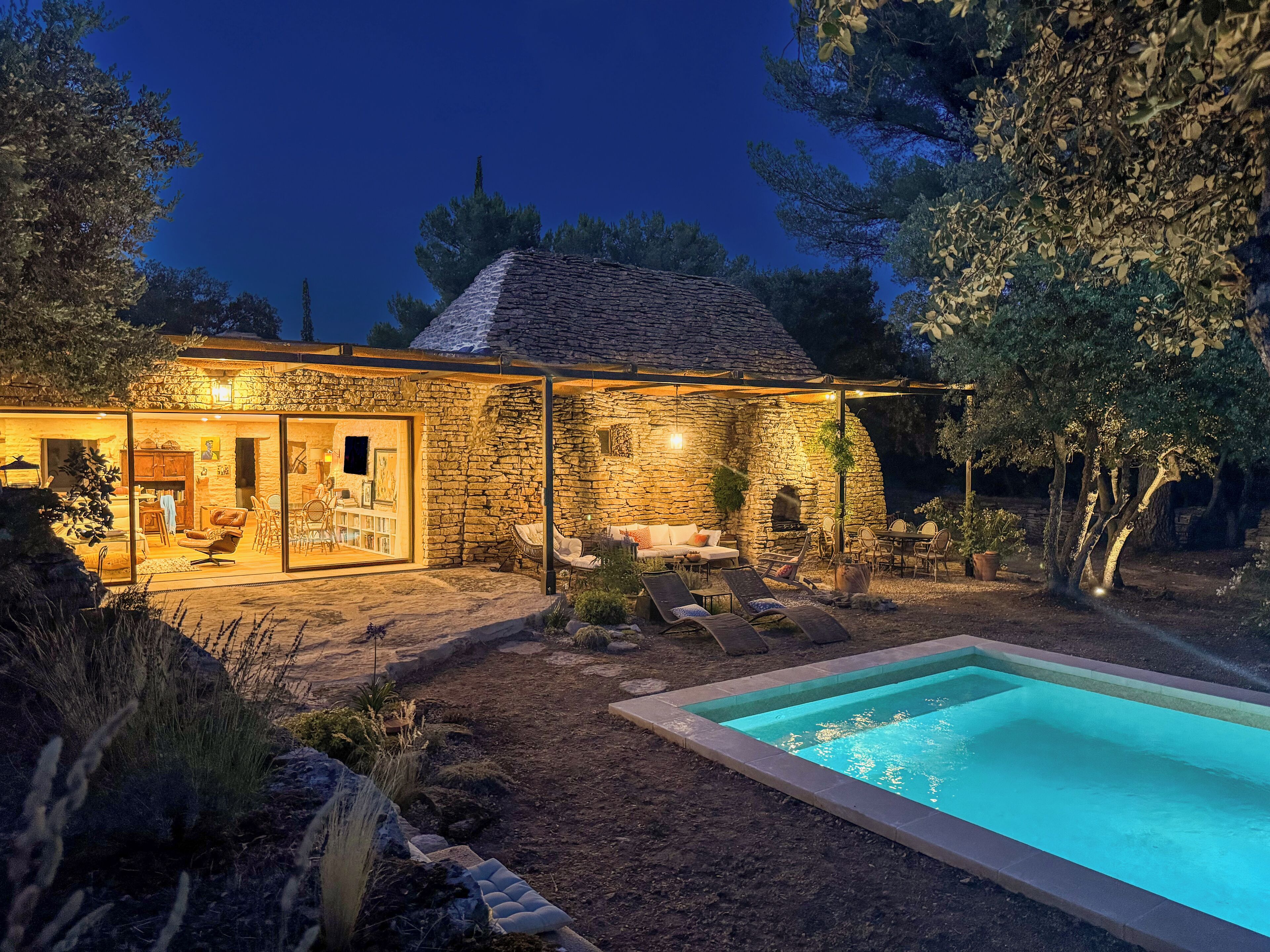 Uma casa de pedra com porta de vidro, área de estar externa e piscina.
