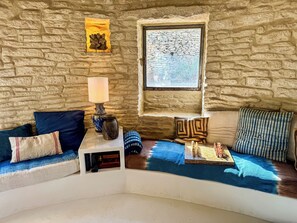A cozy room with a stone wall, a window, a lamp, and a sofa with cushions. - Les Cinq Bories - An Exceptional Estate Just a 10-Minute Walk from the Village of Gordes (Gordes)