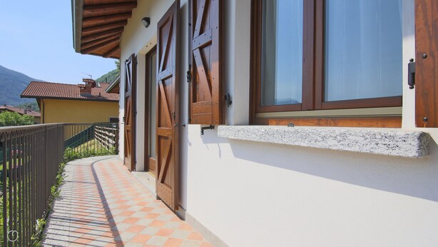 A building with wooden shutters, a tiled pathway, and a mountain in the background. - Villetta Contrada by Wonderful Italy (Cerano D'intelvi)