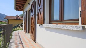 A building with wooden shutters, a tiled pathway, and a mountain in the background. - Villetta Contrada by Wonderful Italy (Cerano D'intelvi)