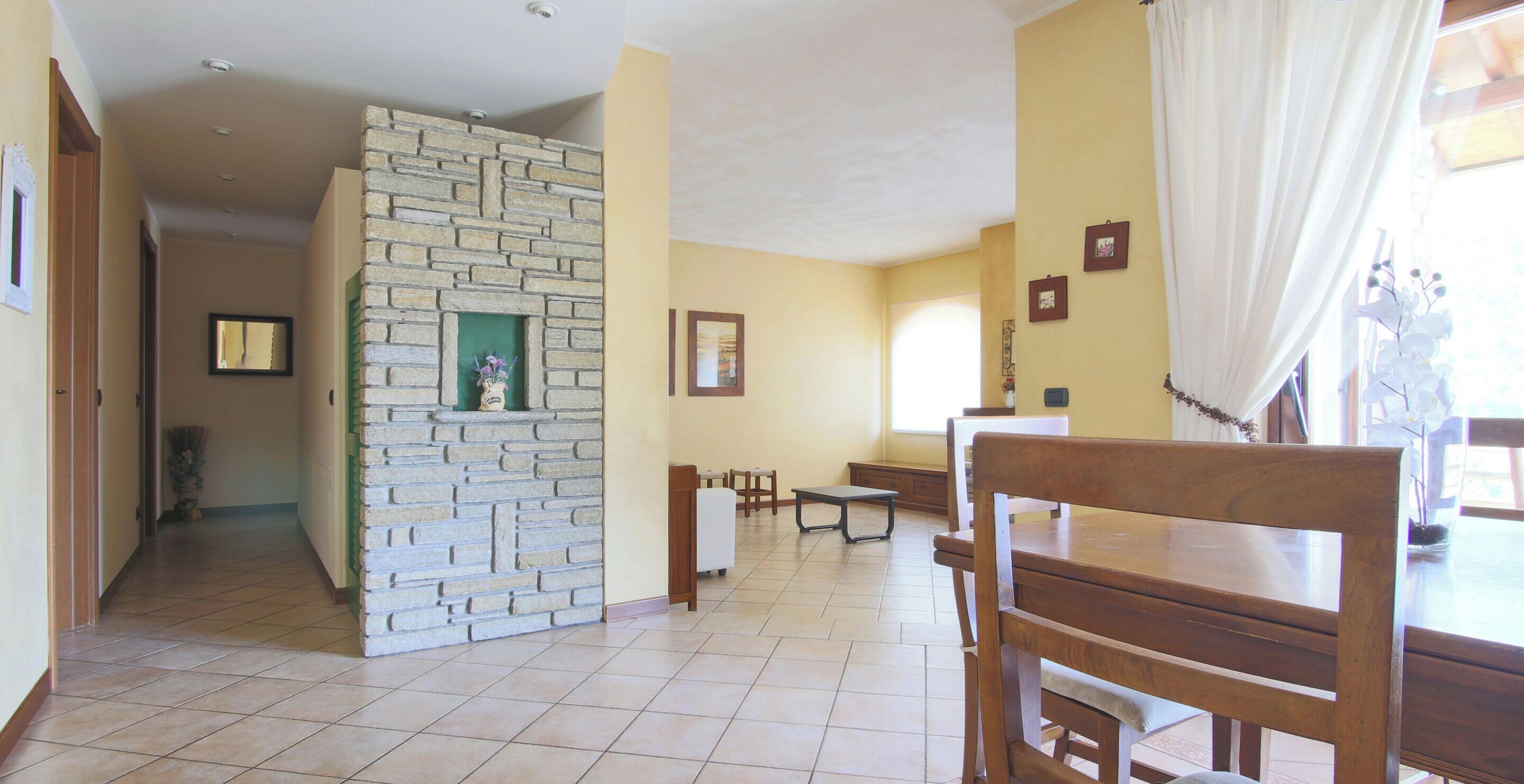A dining area with a stone wall, wooden furniture, and a view of the outside.