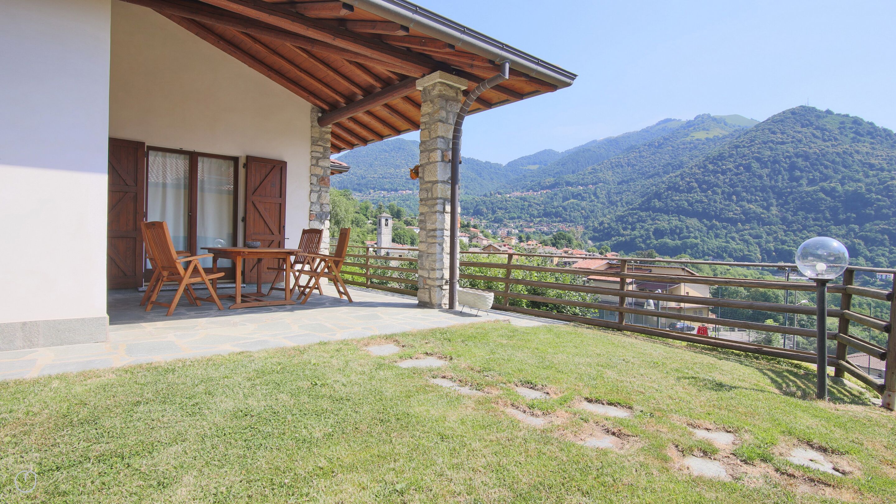 A balcony with a wooden table and chairs, overlooking a mountainous landscape.