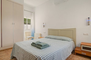 A bedroom with a bed, a chair, a nightstand, a wardrobe, and a window.