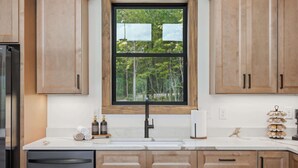 A kitchen with wooden cabinets, a black faucet, a window with blinds, and a white countertop. - NEW Luxury Cabin | Hot Tub+Wet Bar+EV+Mtn Views (Mineral Bluff)