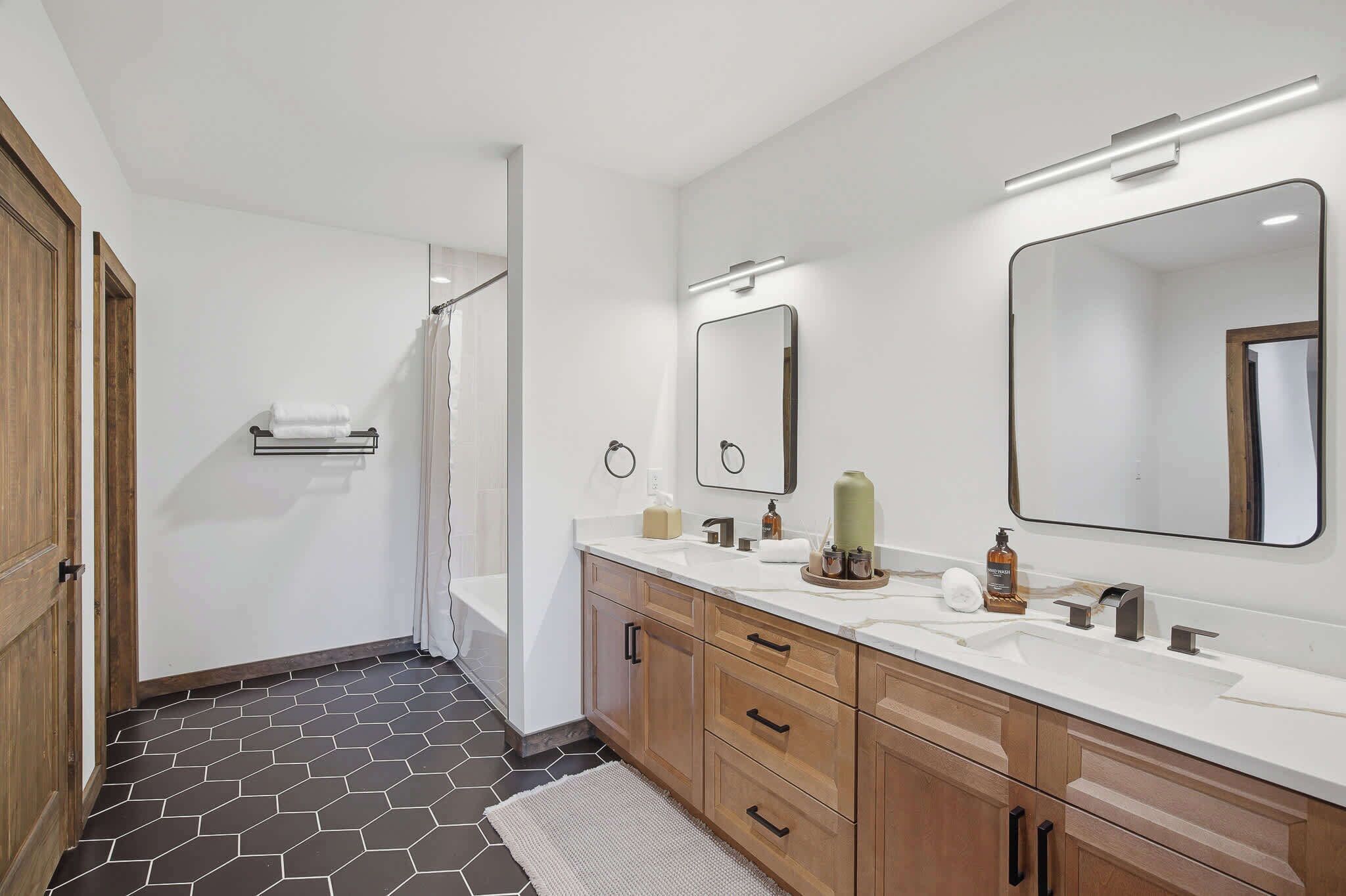 Une salle de bain moderne avec un grand miroir, deux vasques, des meubles en bois et un espace douche.