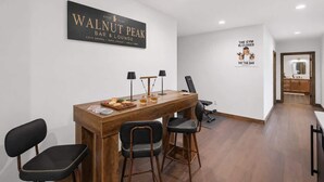 A modern bar/lounge area with a wooden table, chairs, and a sign for Walnut Peak Bar & Lounge. - NEW Luxury Cabin | Hot Tub+Wet Bar+EV+Mtn Views (Mineral Bluff)