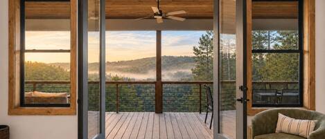 Une pièce avec une terrasse en bois, une chaise et une vue sur un paysage boisé.