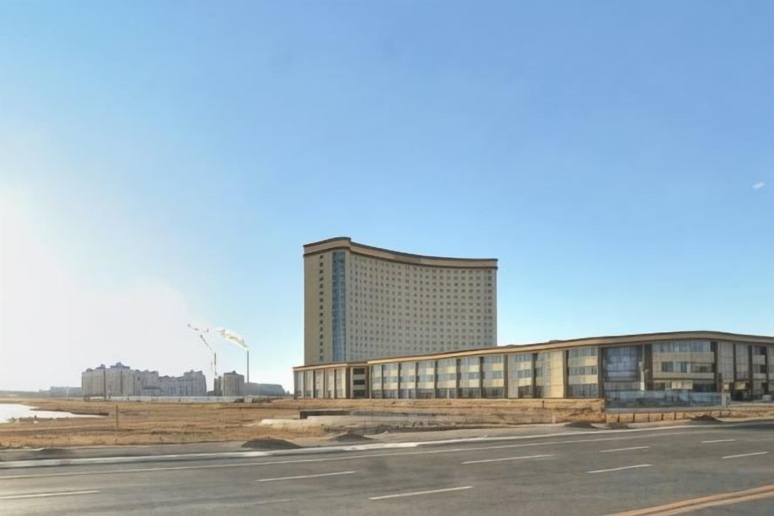 A large building with a curved facade and a flat roof, situated next to a wide road.