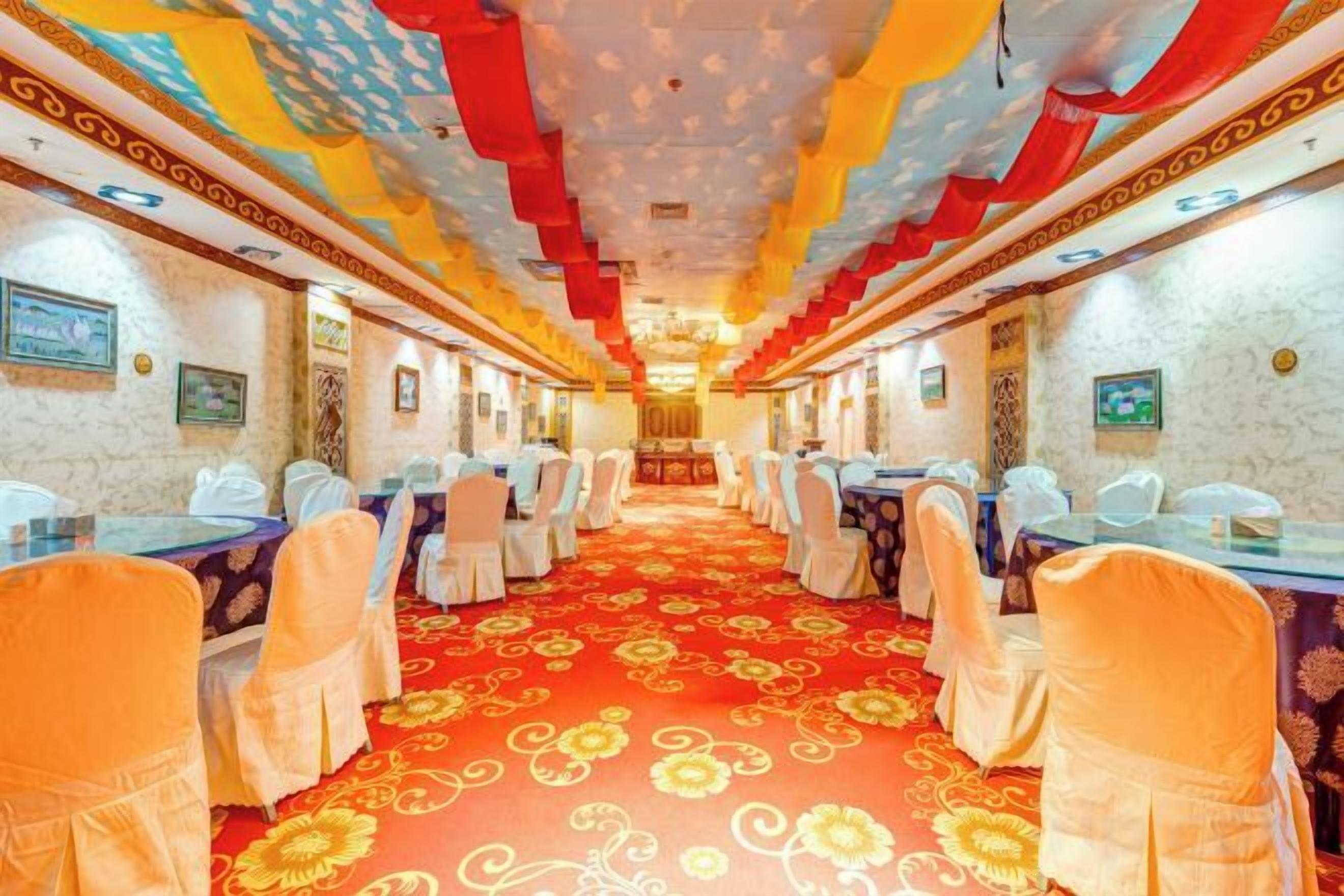 A banquet hall with rows of tables and chairs, a patterned carpet, and a decorative ceiling.
