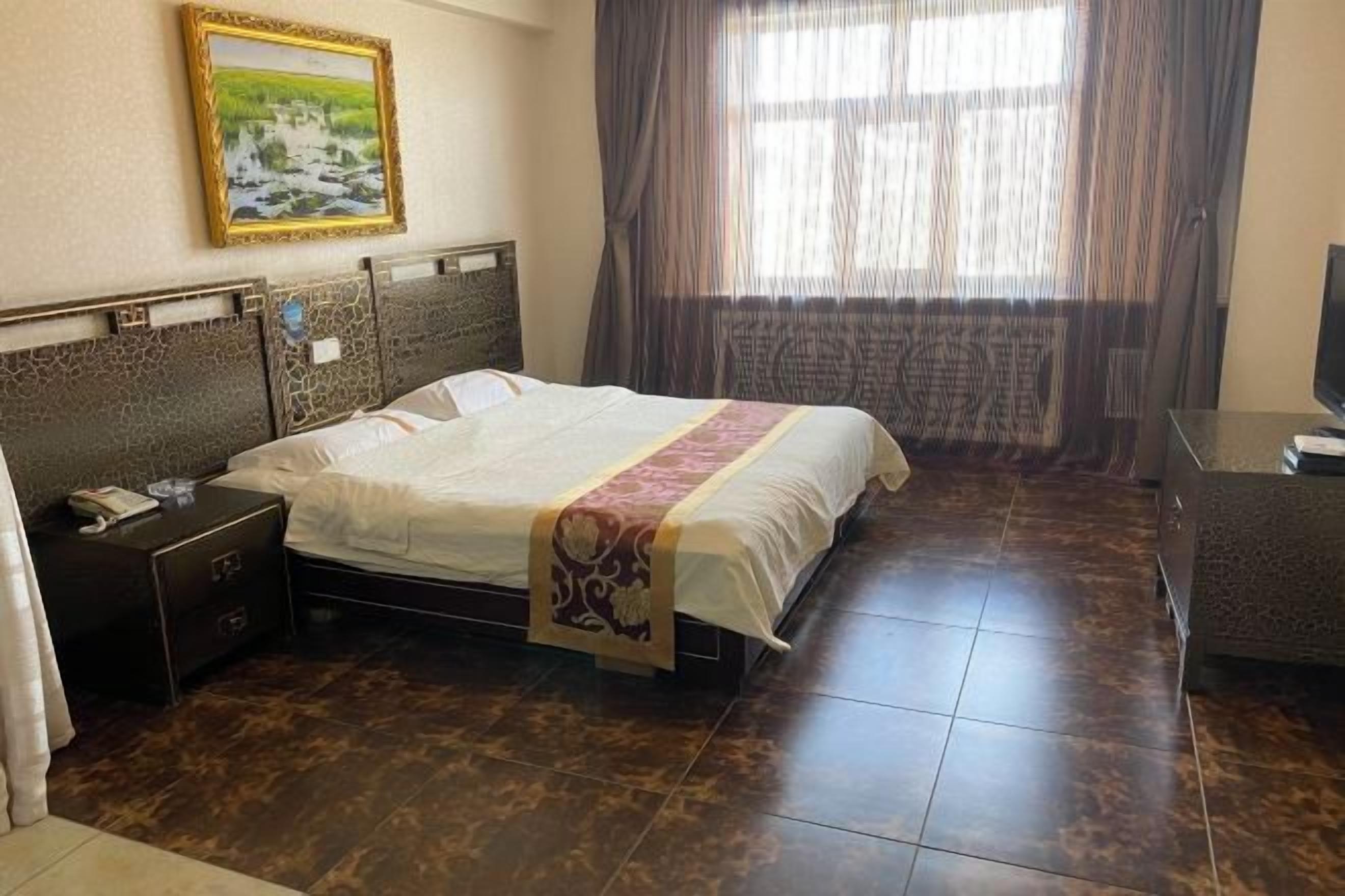 Habitación de hotel con cama, mesita de noche, escritorio, televisor y ventana con cortinas.