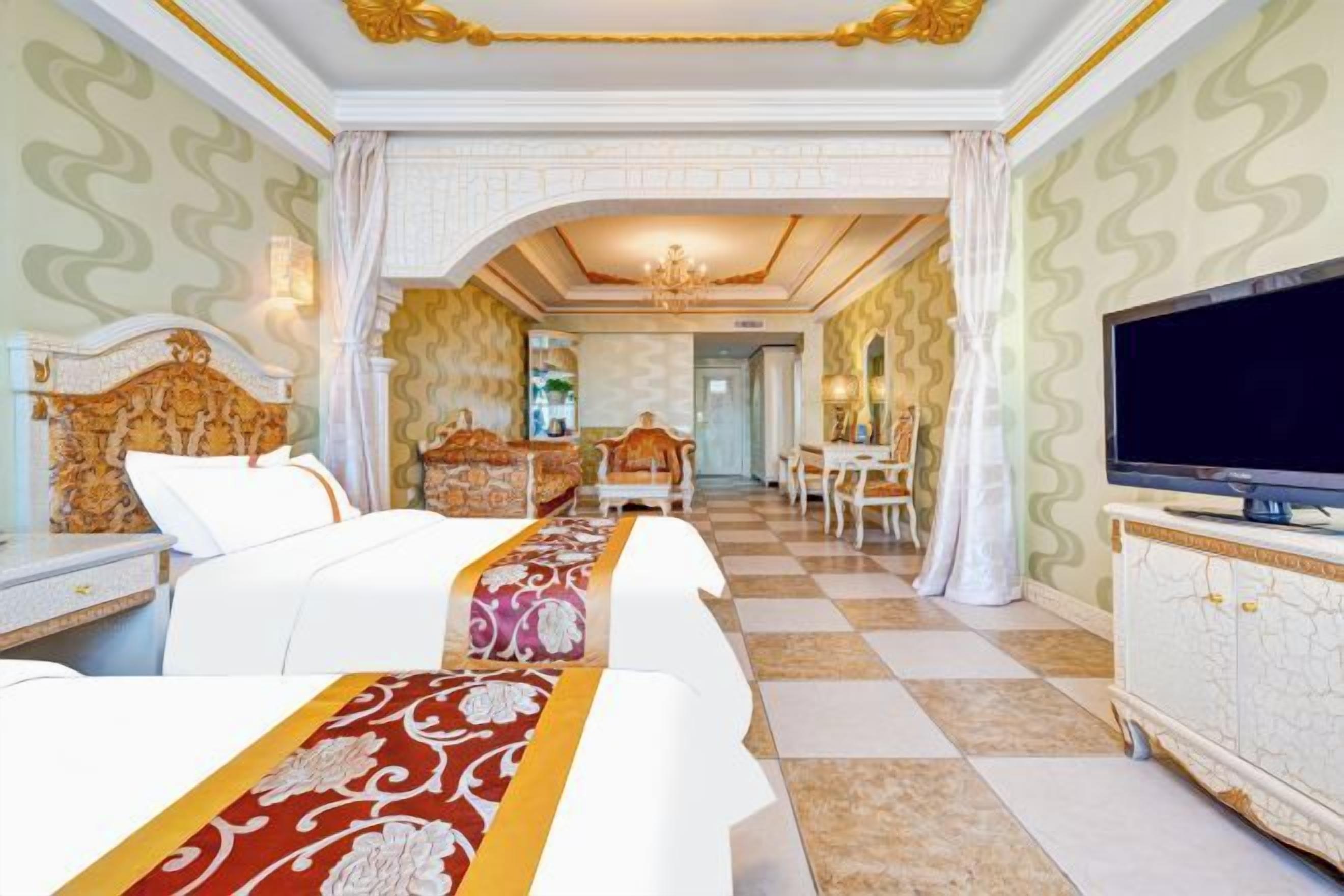 A hotel room with two beds, a television, a dining area, and a bathroom.