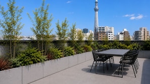 An outdoor terrace with a table and chairs, surrounded by plants and a cityscape in the background. - Minn Asakusa Hanayashiki North (Tokyo)