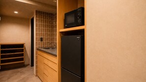 A compact kitchen with a microwave, refrigerator, and wooden shelving unit. - Minn Asakusa Hanayashiki North (Tokyo)