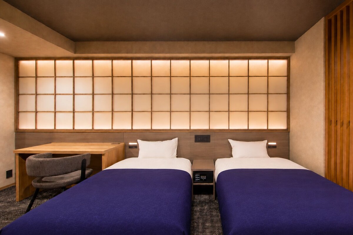 A hotel room with two beds, a desk, and a chair.