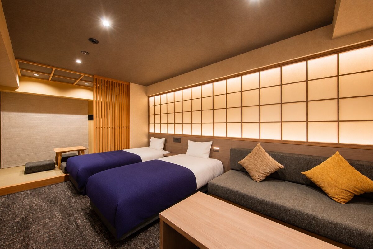 A hotel room with two beds, a sofa, a TV, and a sliding shoji screen.