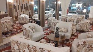 Eine Hotelhalle mit mehreren Sitzbereichen, einem gemusterten Teppich und Blick auf die Straße durch große Fenster.