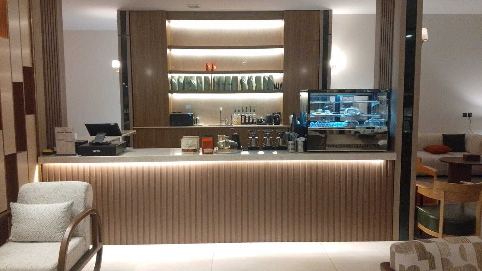 Un espace bar moderne avec un comptoir, des tabourets de bar et un téléviseur diffusant des images d’un concessionnaire automobile.