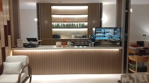 A modern bar area with a counter, bar stools, and a television displaying a car showroom. - Al Waal Al Khafji Hotel (Al Khafji)