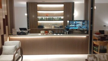 A modern bar area with a counter, bar stools, and a television displaying a car showroom.