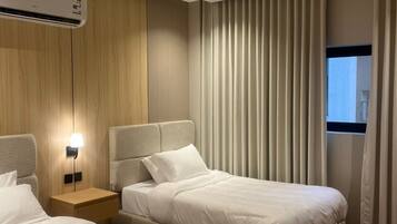 Ein Hotelzimmer mit zwei Betten, einem Nachttisch, einer Klimaanlage und einem Fenster mit Vorhängen.