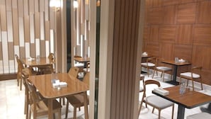 Ein moderner Essbereich mit Holztischen und -stühlen, einer Trennwand mit vertikalen Lamellen und einer Holzwand.