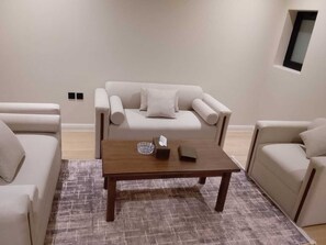 Una sala de estar con un sofá, dos sillones, una mesita de centro y un ventanal pequeño.