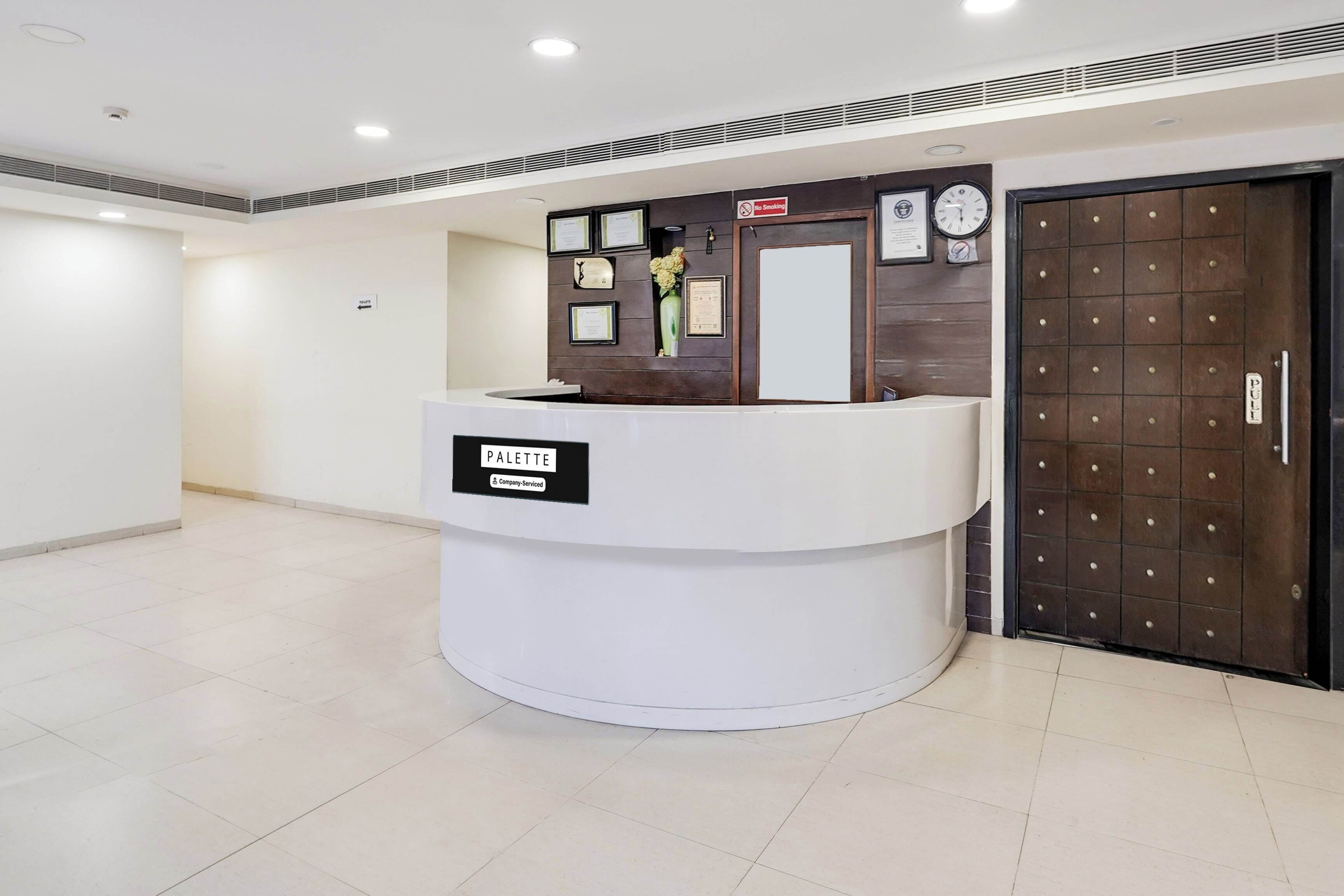 A reception desk with a sign reading 'PALETTE & Company Services,' a clock, framed certificates, and a door with a metal grid pattern.