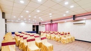 A conference room with rows of chairs covered in yellow and red, a ceiling with recessed lighting, and an air conditioning unit on the wall. - Palette Country Club Surat (Surat)