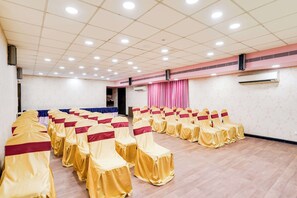 A conference room with rows of chairs covered in yellow and red, a ceiling with recessed lighting, and an air conditioning unit on the wall.