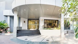 A modern building with a curved entrance, steps leading up to a glass door, and potted plants around the entrance area. - Palette Country Club Surat (Surat)