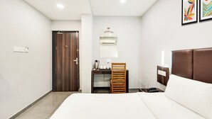 A hotel room with a bed, a desk with a chair, a wardrobe, a mirror, and a wall-mounted air conditioning unit. - Palette Country Club Surat (Surat)