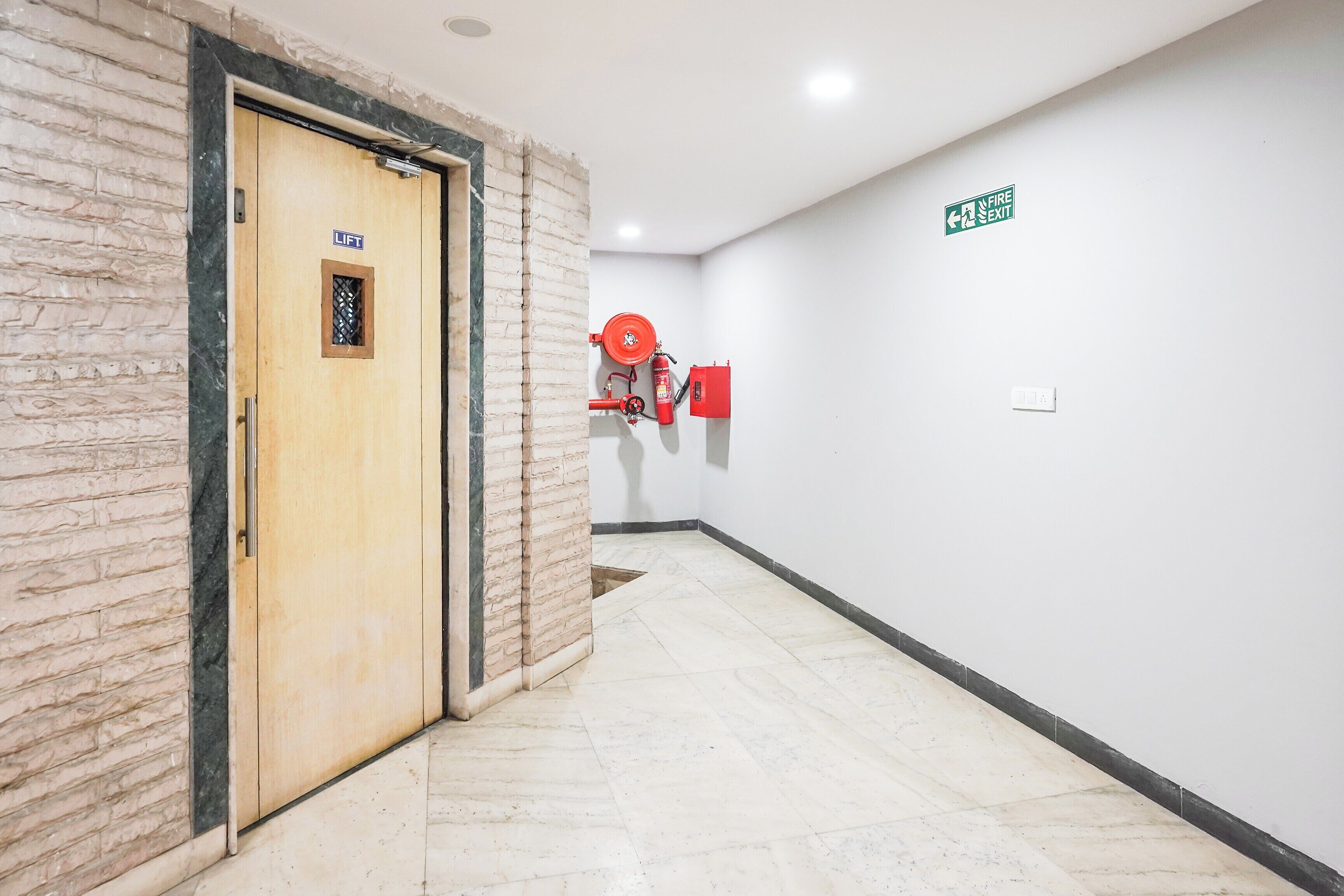Un pasillo con una señal de salida de incendios, un extintor montado en la pared y una puerta con señal de ascensor.